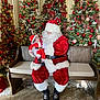 baby, child, santa_claus, christmas_trees, holiday, bench, red_clothing, white_fur_trim, decorations, ribbons, candy_canes, lights, festive, indoor, floor, wood, smiling, person, seasonal, celebration