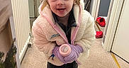 Layana is registered to the contest to win money with this photo: bottle, carpet, child, christmas_tree, clothing, crown, door, floor, footwear, gloves, happy, holiday, indoor, jacket, person, pink, shoes, smiling, toddler, toy