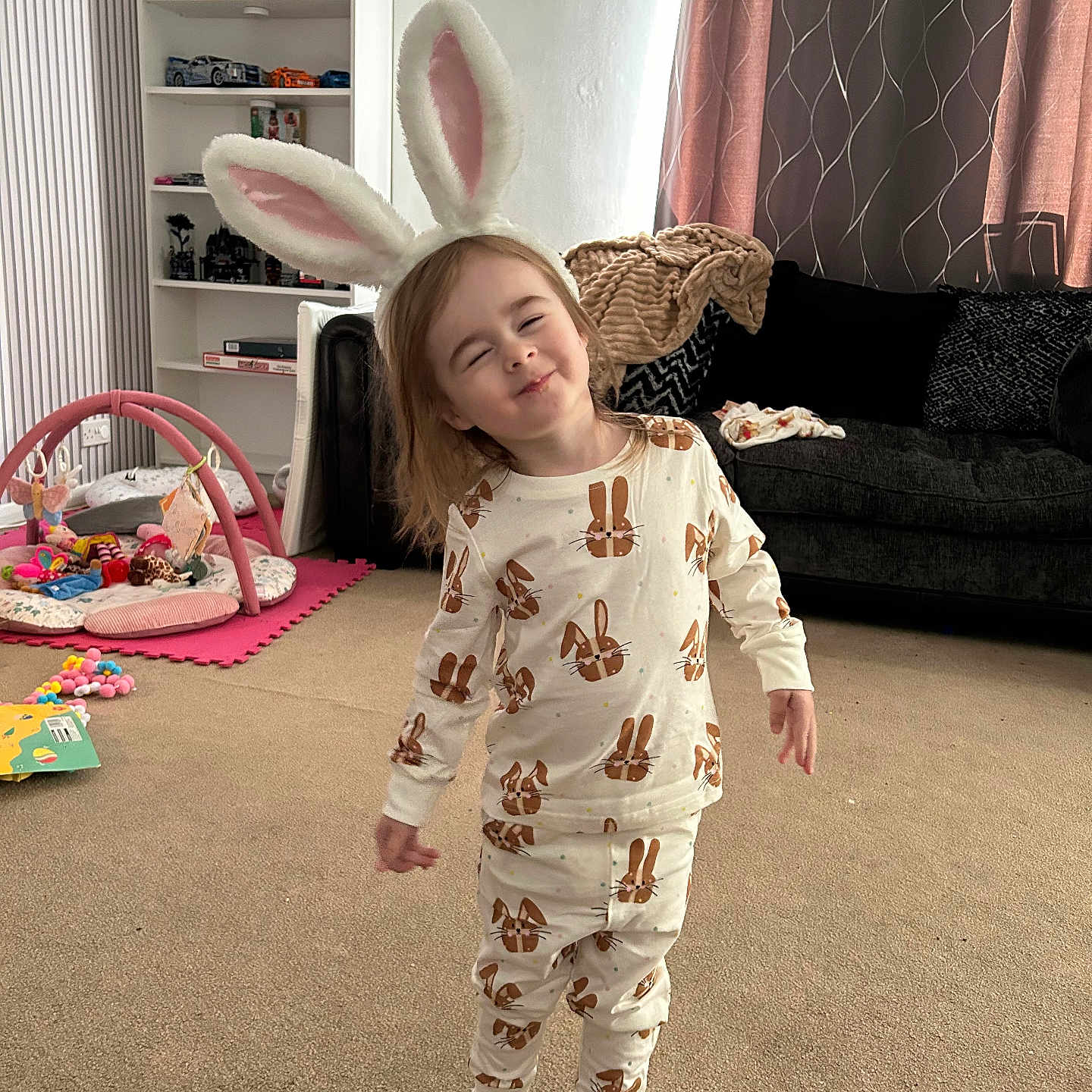 Layana joined the competition — help win amazing prizes! child, bunny_ears, pajamas, indoor, living_room, carpet, toys, smiling, barefoot, curtains, couch, blanket, shelf, play_mat, person, cute, happy, young_child, home, fun