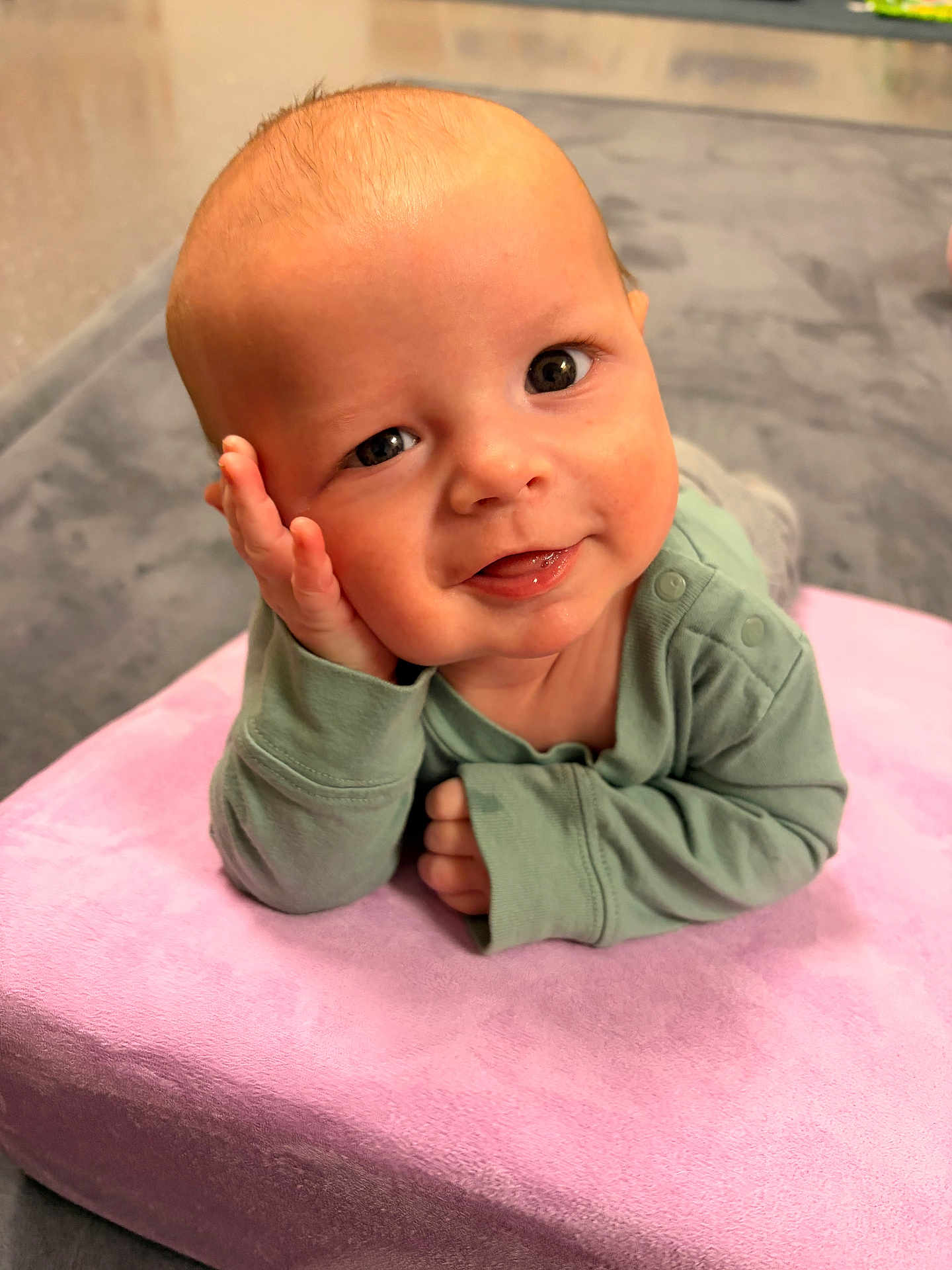 Hudson is registered to the contest to win money with this photo: baby, infant, child, smile, face, hand, cushion, pink, green_clothing, long_sleeves, indoors, portrait, cute, resting, head_support, closeup, soft_texture, happy, person, toddler