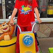 Eerika Lyhn West is registered to the contest to win money with this photo: amusement, background, building, cartoon_bear, casual, child, daylight, fun, girl, kiddie_ride, outdoor, person, playful, playground, red_clothing, smiling, sneakers, toy, window, yellow_motorcycle