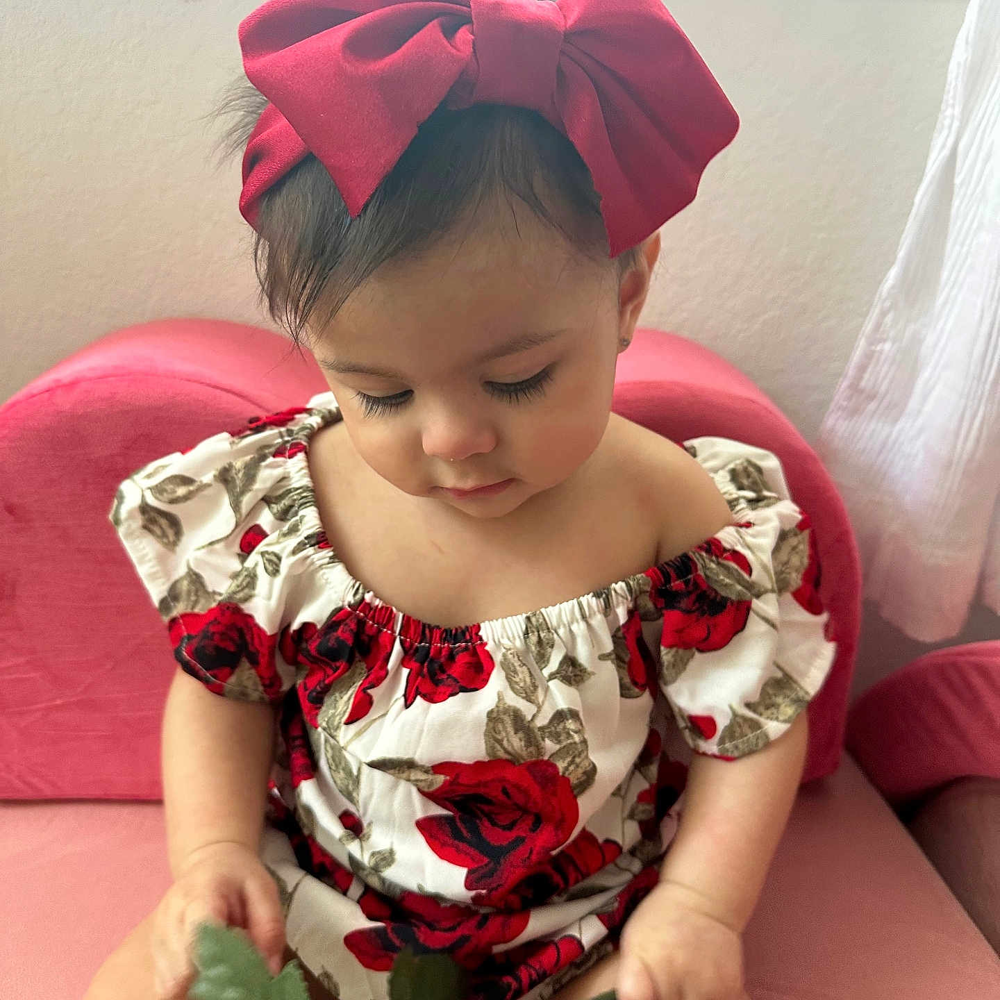 Selena joined the competition — help win amazing prizes! baby, bow, child, curtain, cute, floral_dress, flower_pattern, green_leaf, home, indoor, long_eyelashes, looking_down, person, pink_chair, plant_stem, red_bow, short_hair, sitting, soft_light, toddler