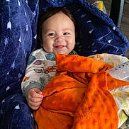 Tristan joined the competition — help win amazing prizes! baby, blanket, blue_blanket, orange_blanket, baby_seat, pajamas, smiling, infant, indoor, toy, gnome, face, hand, cozy, floor, carpet, child, comfort, cute, portrait