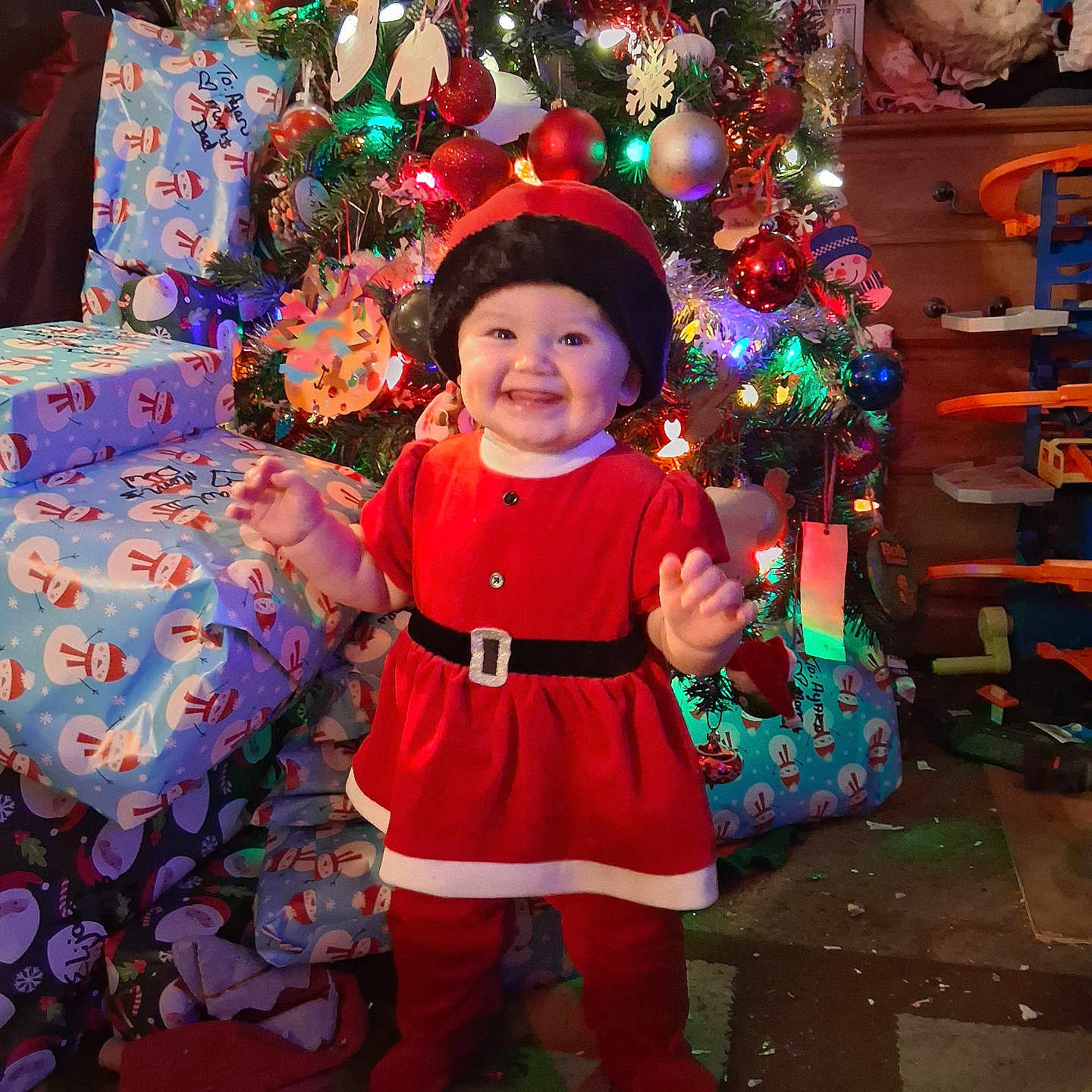 Ayaru joined the competition — help win amazing prizes! baby, carpet, celebration, child, christmas_tree, decorations, festive, floor, furniture, gift_wrap, happy, holiday, indoors, lights, ornaments, presents, red_dress, santa_hat, smiling, toy