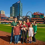 Ayaru is registered to the contest to win money with this photo: family, baseball_field, stadium, group, people, children, adults, grass, sky, buildings, arch, outdoor, sunny, casual_clothing, smiling, child, baby, woman, man, portrait