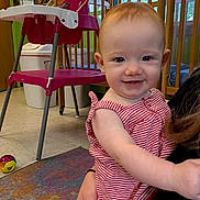 Sophia is registered to the contest to win money with this photo: toddler, child, smiling, red_hair, striped_clothing, indoor, high_chair, ball, carpet, daycare, playroom, person, baby, holding, furniture, window, toy, colorful, happy, face