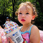 Savannah is registered to the contest to win money with this photo: toddler, child, curly_hair, pink_clothing, cinnamon_toast_crunch, container, outdoor, forest, trees, sunlight, summer, portrait, cute, food, snack, holding, nature, daylight, person, young_child