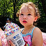 toddler, child, curly_hair, pink_clothing, cinnamon_toast_crunch, container, outdoor, forest, trees, sunlight, summer, portrait, cute, food, snack, holding, nature, daylight, person, young_child