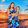 woman, child, toddler, dress, floral_pattern, beach, sunset, ocean, waves, palm_tree, smile, happy, outdoor, nature, sky, clouds, water, sand, family, vacation