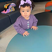Dahlia is registered to the contest to win money with this photo: blanket, child, clothing, couch, curly_hair, cute, eyes, face, floor, furniture, hands, headband, indoor, living_room, modern, person, portrait, purple_sweatshirt, table, toddler