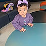 blanket, child, clothing, couch, curly_hair, cute, eyes, face, floor, furniture, hands, headband, indoor, living_room, modern, person, portrait, purple_sweatshirt, table, toddler