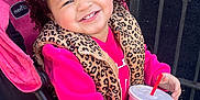 Dahlia is registered to the contest to win money with this photo: black_leggings, bow, brick_wall, child, cup, curly_hair, daylight, drink, fast_food, happy, iron_fence, leopard_print, outdoor, pink, sidewalk, smile, sneakers, stroller, toddler, vest