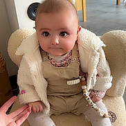 Alba a rejoint le concours — aidez-le/la à gagner de superbes lots ! baby, infant, child, plush_chair, white_fleece_jacket, overalls, floral_top, pacifier_clip, beaded_chain, fringe_boots, tights, holding_hand, wide_eyes, chubby_cheeks, cute_expression, indoor, kitchen_background, speaker, floor, soft_lighting