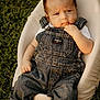 baby, denim_overalls, infant, grass, outdoor, seat, white_cushion, cute, child, portrait, thinking, casual_wear, barefoot, skin, head, hand, foot, person, nature, sunlight
