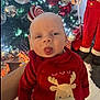 baby, child, christmas_tree, ornaments, holiday, festive, red_clothing, reindeer, tongue_out, cute, indoor, person, celebration, smile, christmas_decorations, toy, holiday_lights, seasonal, festivity, infant