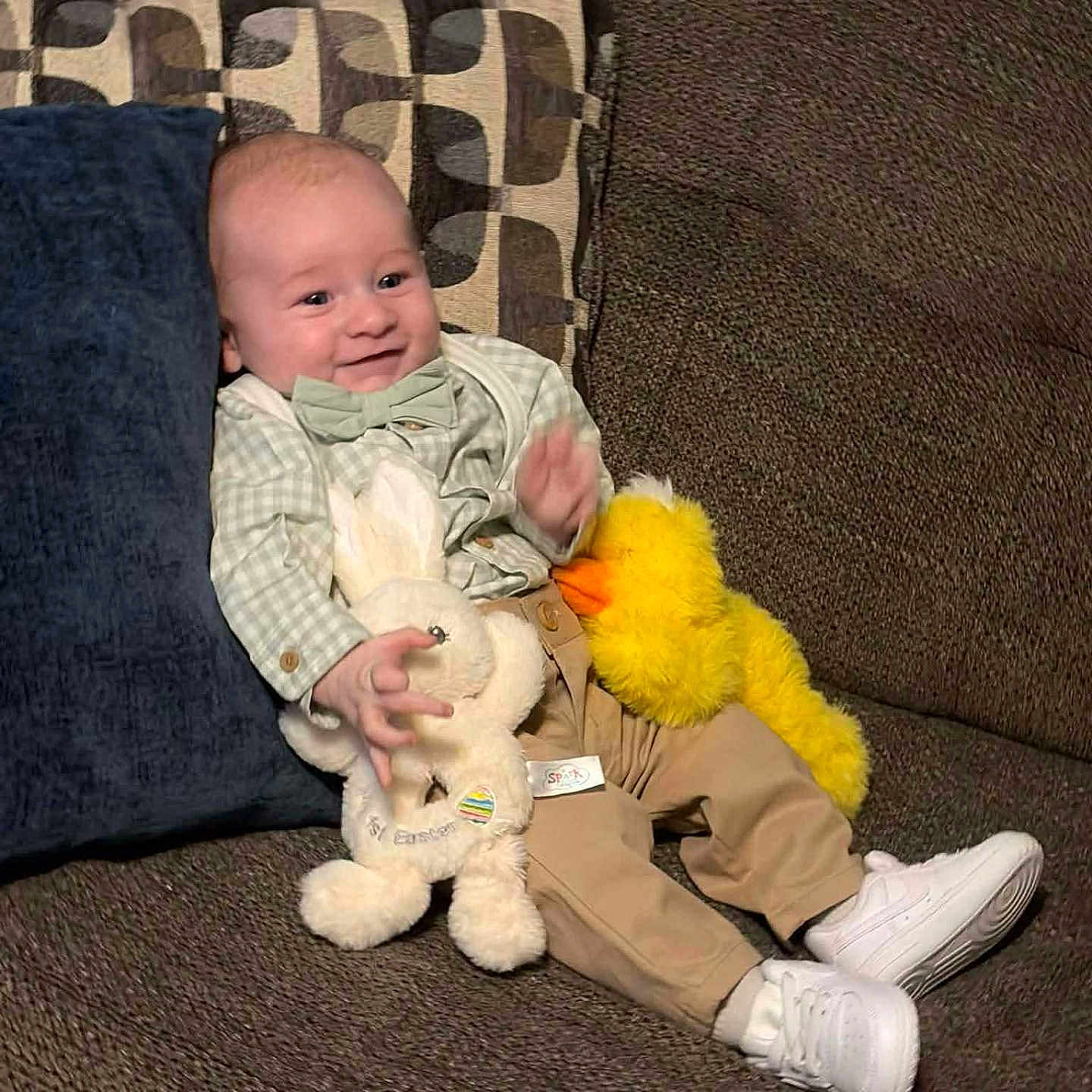 Dominic joined the competition — help win amazing prizes! baby, child, smiling, couch, plush_toy, stuffed_animal, bunny, duck, bow_tie, shirt, pants, sneakers, pillow, cushion, indoor, happy, person, seated, comfortable, cute