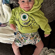 George joined the competition — help win amazing prizes! baby, child, smiling, hoodie, cartoon_character, shorts, socks, blanket, couch, indoor, person, face, happy, cute, infant, clothing, comfort, relaxing, playful, soft