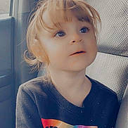 Bexley joined the competition — help win amazing prizes! child, toddler, car_seat, seat, clothing, shirt, text_on_clothing, rainbow_colors, long_sleeves, hair, face, eyes, expression, indoors, car_interior, window, seatbelt_slot, portrait, cute, curly_hair