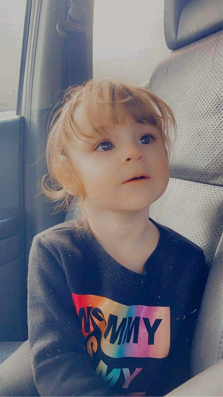 Bexley joined the competition — help win amazing prizes! child, toddler, car_seat, seat, clothing, shirt, text_on_clothing, rainbow_colors, long_sleeves, hair, face, eyes, expression, indoors, car_interior, window, seatbelt_slot, portrait, cute, curly_hair