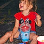 beverage, candy, child, drink, face, food, fun, happy, laughing, night, outdoor, pavement, person, plastic_cup, playful, red_shirt, shorts, sitting, snack, straw