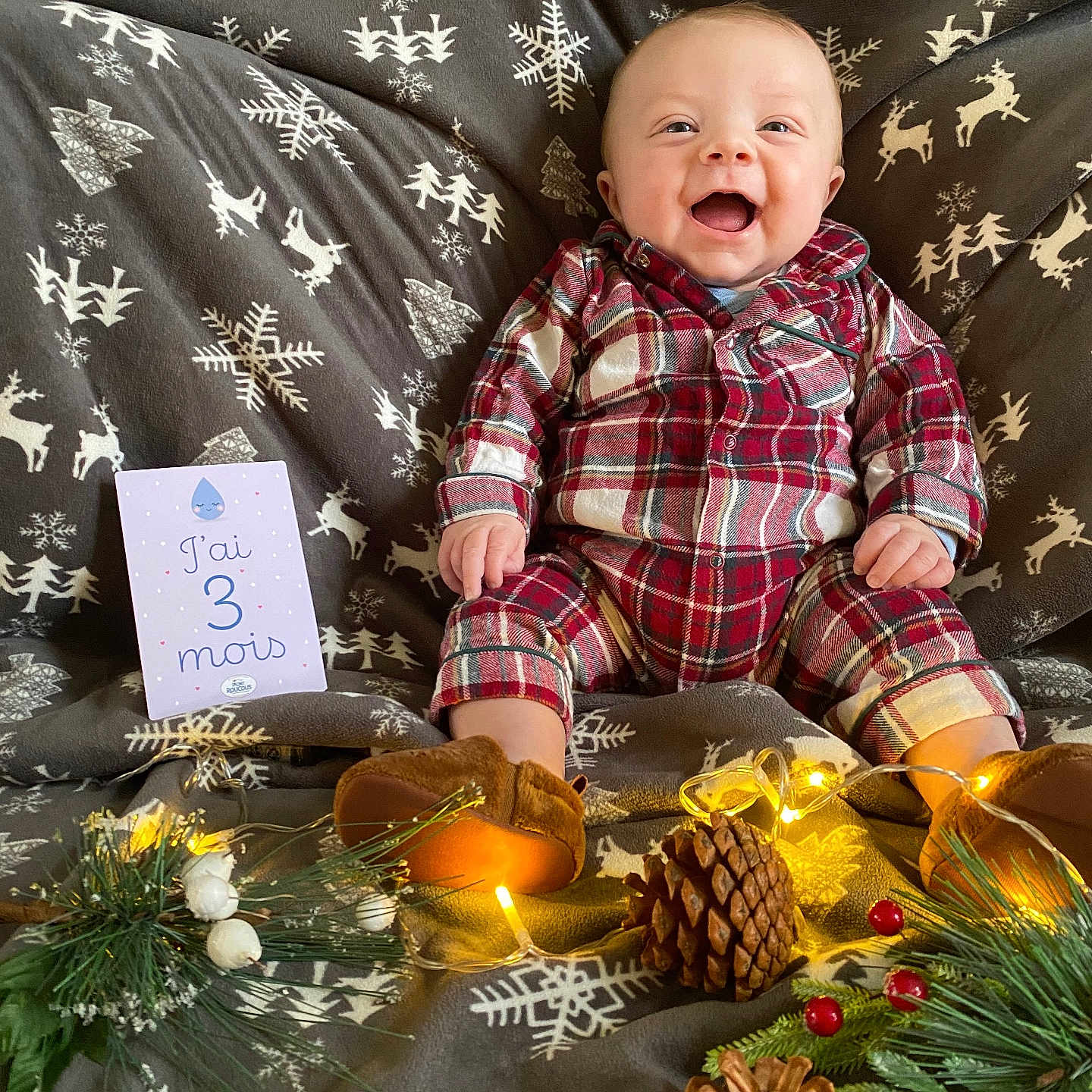 Arthur participe au concours pour gagner de l'argent avec cette photo : baby, blanket, celebration, cozy, cute, fairy_lights, festive, greenery, holiday, indoor, infant, pine_cone, plaid_pajamas, portrait, reindeer_pattern, sitting, smiling, snowflake_pattern, toe_shoes, warm_lighting