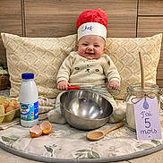 Arthur participe au concours pour gagner de l'argent avec cette photo : baby, blanket, chef_hat, cute, eggshells, flour, happy, jar, kitchen_props, milestone_card, milk_bottle, mixing_bowl, onesie, pillow, portrait, sitting, smiling, whisk, wood_paneling, wooden_spoon