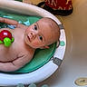baby, bathtub, water, toy, turtle_toy, green_cushion, bathroom, child, infant, skin, face, eyes, head, water_droplets, towel, dinosaur_towel, relaxing, bath_time, cute, indoors