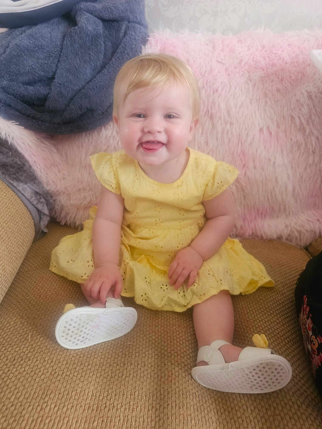 Evie-Jo joined the competition — help win amazing prizes! baby, child, yellow_dress, smiling, sitting, white_sandals, couch, blanket, soft_texture, happy, indoor, cute, playful, infant, person, portrait, cozy, furniture, blonde_hair, casual