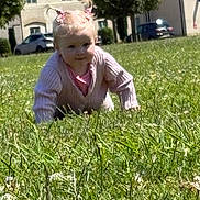 Evie-Jo is registered to the contest to win money with this photo: toddler, child, grass, outdoor, crawling, pink_sweater, pigtails, greenery, daylight, houses, cars, nature, playing, cute, young_child, person, field, sunlight, casual_clothing, exploration