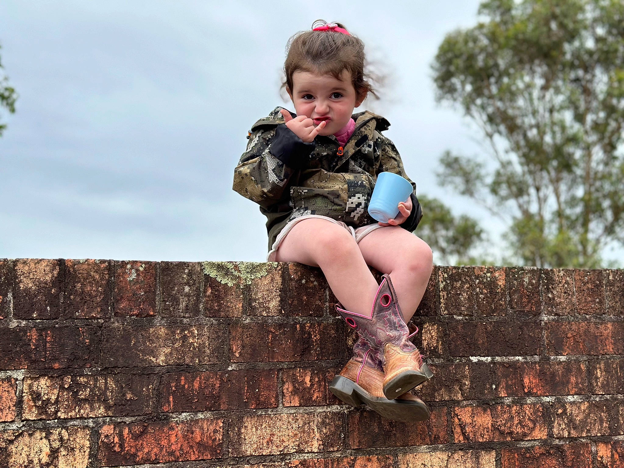 Maddison is registered to the contest to win money with this photo: blond, boot, brick, brickwork, eye, face, flash_photography, fun, grass, happy, human_leg, knee, leisure, people_in_nature, person, sitting, sky, smile, thigh, toddler
