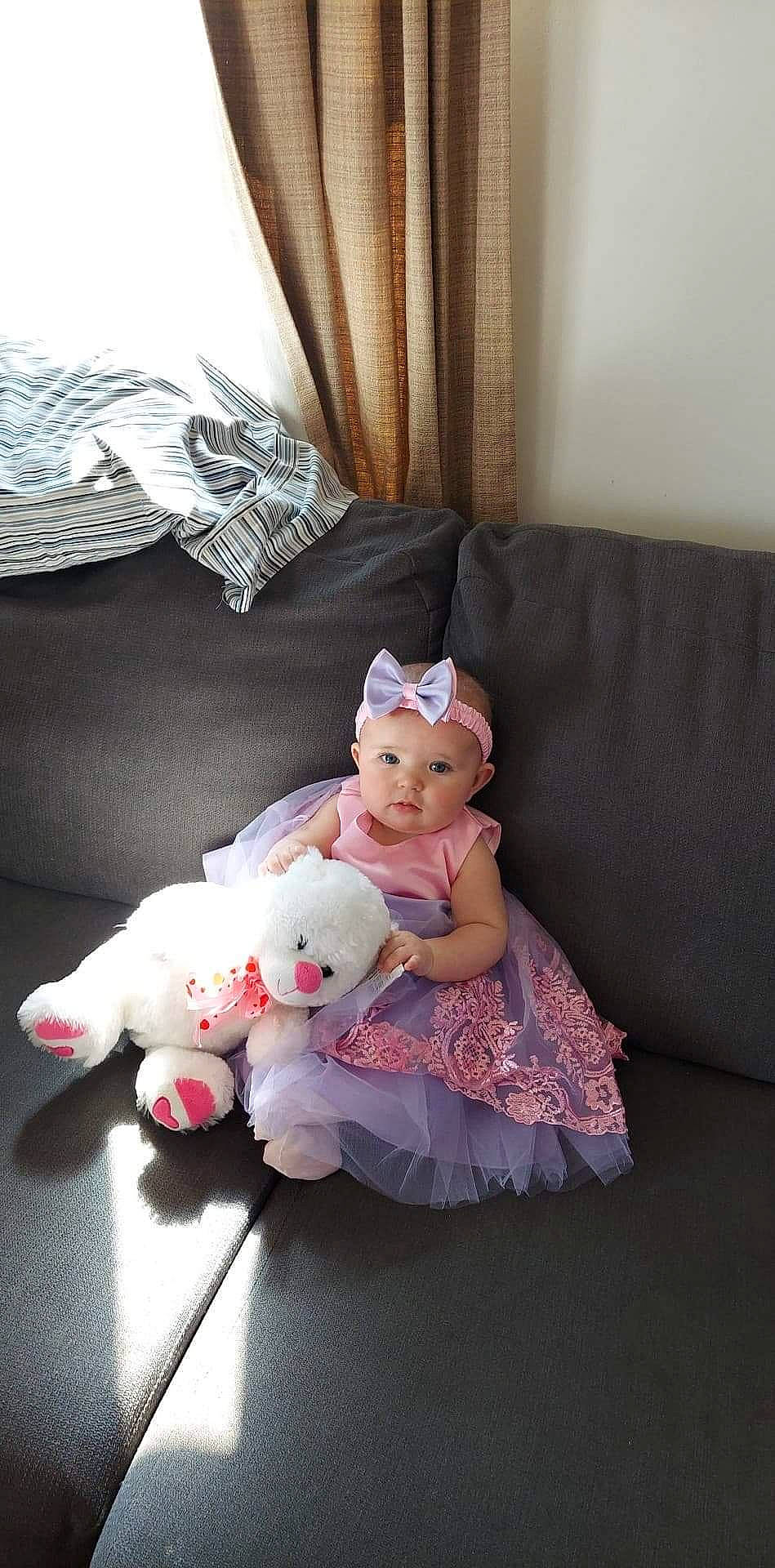 Emma joined the competition — help win amazing prizes! baby, child, comfort, couch, curtain, doll, headwear, lap, linens, living_room, person, pink, plush, room, sitting, stuffed_toy, teddy_bear, textile, toddler, toy
