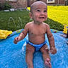 baby, child, pool, water, splashing, smiling, outdoor, grass, sunny, brick_house, blue_swim_diaper, summer, happy, sitting, toes, skin, person, daylight, play, fun