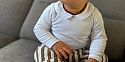 Awen a rejoint le concours — aidez-le/la à gagner de superbes lots ! toddler, child, baby, couch, sofa, clothing, white_shirt, striped_pants, socks, indoor, portrait, sitting, cute, curious, young_child, person, face, hands, feet, home