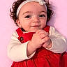 Lillyonna joined the competition — help win amazing prizes! baby, child, infant, curly_hair, headband, flower, red_dress, white_shirt, hand_clasp, smiling, portrait, pink_background, cute, person, young_child, closeup, happy, indoor, toddler, fashion