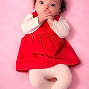 Lillyonna joined the competition — help win amazing prizes! baby, infant, red_dress, white_tights, headband, flower_headband, curly_hair, pink_background, lying_down, hands_near_mouth, wide_eyes, cute, adorable, child, portrait, soft_texture, studio_photo, young_child, expression, clothing