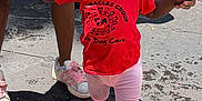 Kaylani is registered to the contest to win money with this photo: toddler, child, red_shirt, pink_slippers, daycare, outdoor, holding_hands, walking, sunlight, shadow, concrete_floor, adult_hands, shorts, curly_hair, playground, people, support, casual_clothing, footwear, summer