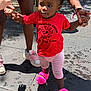 toddler, child, red_shirt, pink_slippers, daycare, outdoor, holding_hands, walking, sunlight, shadow, concrete_floor, adult_hands, shorts, curly_hair, playground, people, support, casual_clothing, footwear, summer