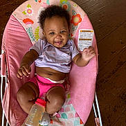 Katyria is registered to the contest to win money with this photo: baby, smile, happy, pink, bottle, baby_chair, wooden_floor, clothing, cute, infant, person, sitting, waving, indoors, colorful, playful, tongue_out, short_sleeve, diaper, sock