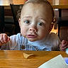 baby, child, infant, portrait, face, eyes, wide_eyed, sitting, restaurant, dining_table, wooden_table, highchair, bib, white_shirt, food, tortilla_chip, hands, indoor, candid, cute