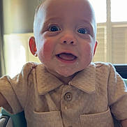 Eli is registered to the contest to win money with this photo: baby, beige_shirt, buttoned_shirt, child, cute, drool, face, happy, high_chair, indoor, infant, natural_light, person, portrait, short_hair, sitting, skin, smiling, window, young_child