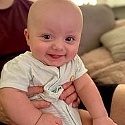 Nathaniel is registered to the contest to win money with this photo: baby, smiling, tongue_out, infant, person, hand, clothing, seated, indoor, couch, adult_hand, cute, happy, portrait, face, skin, young_child, cozy, home, bright_eyes