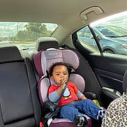 Kingslin is registered to the contest to win money with this photo: toddler, child, car_seat, car_interior, seatbelt, red_shirt, blue_jeans, penguin_graphic, leopard_print, window, car, road, trees, sky, clouds, seat, socks, finger_in_mouth, safety, baby