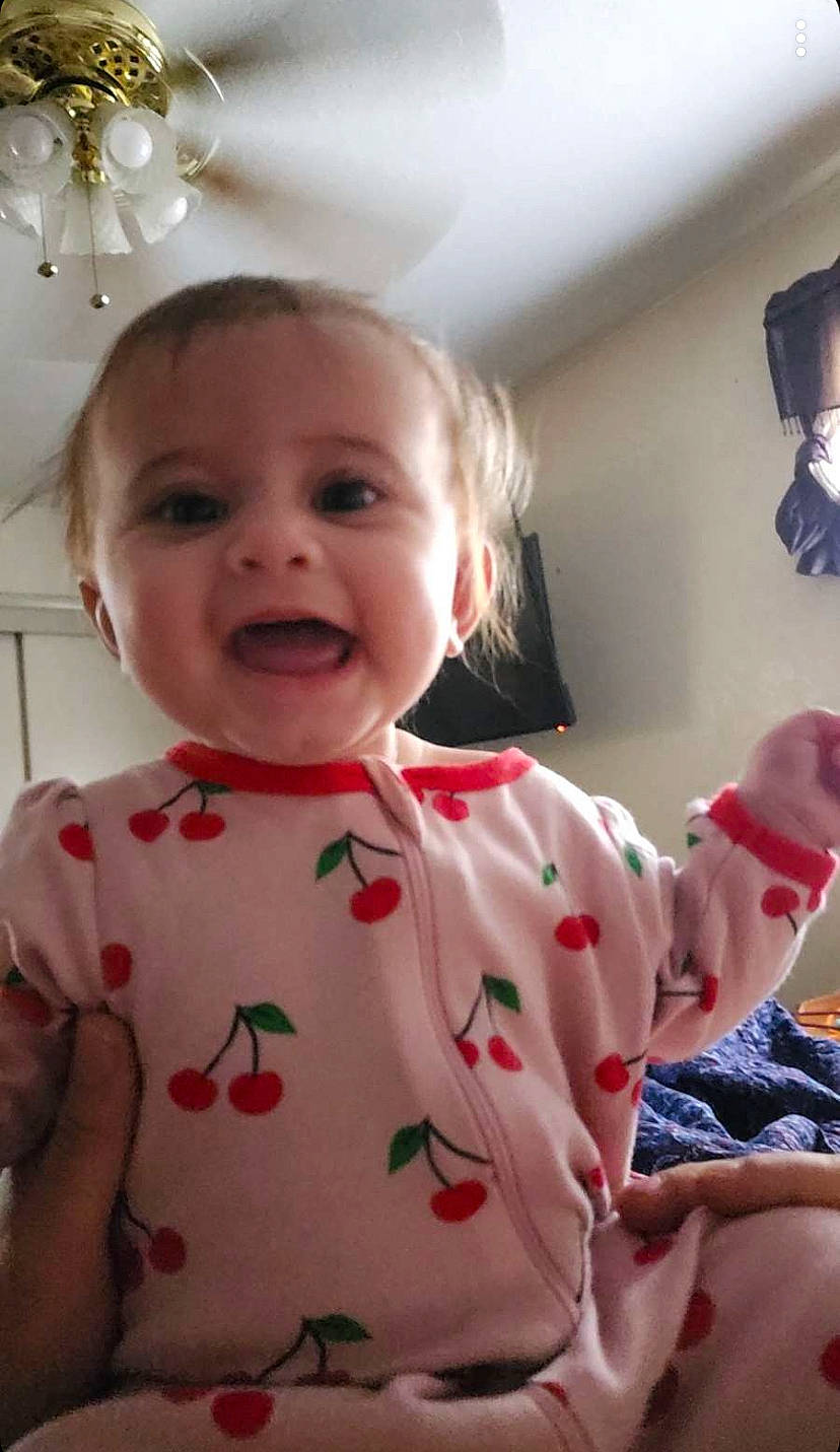 Scarlett is registered to the contest to win money with this photo: baby, baby_toddler_clothing, cheek, child, eye, finger, fun, happy, lamp, lip, pattern, person, pink, room, skin, sleeve, smile, standing, t_shirt, toddler