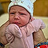 baby, infant, hands, pink_clothing, hat, cute, newborn, bracelets, closeup, portrait, indoor, soft_lighting, expression, skin, person, child, face, headwear, sleeves, holding