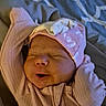 baby, newborn, infant, sleeping, pink_clothing, hat, smile, arms_up, blanket, bed, indoors, cute, soft_lighting, resting, child, portrait, peaceful, cozy, warm, closeup