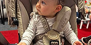 Anaelle participe au concours pour gagner de l'argent avec cette photo : baby, child, stroller, pajamas, indoor, seatbelt, curious, toy, play_area, infant, clothing, person, face, hand, red_carpet, fabric, seat, looking_away, cute, young_child