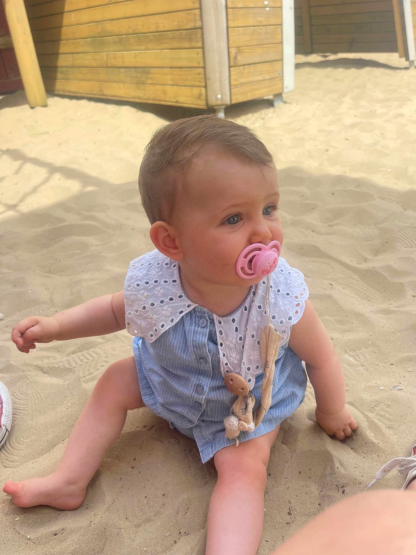 Anaelle a rejoint le concours — aidez-le/la à gagner de superbes lots ! baby, pacifier, sand, child, outdoor, blue_outfit, white_collar, wooden_structure, sitting, barefoot, cute, infant, sunlight, play_area, summer, toy, closeup, portrait, skin, person