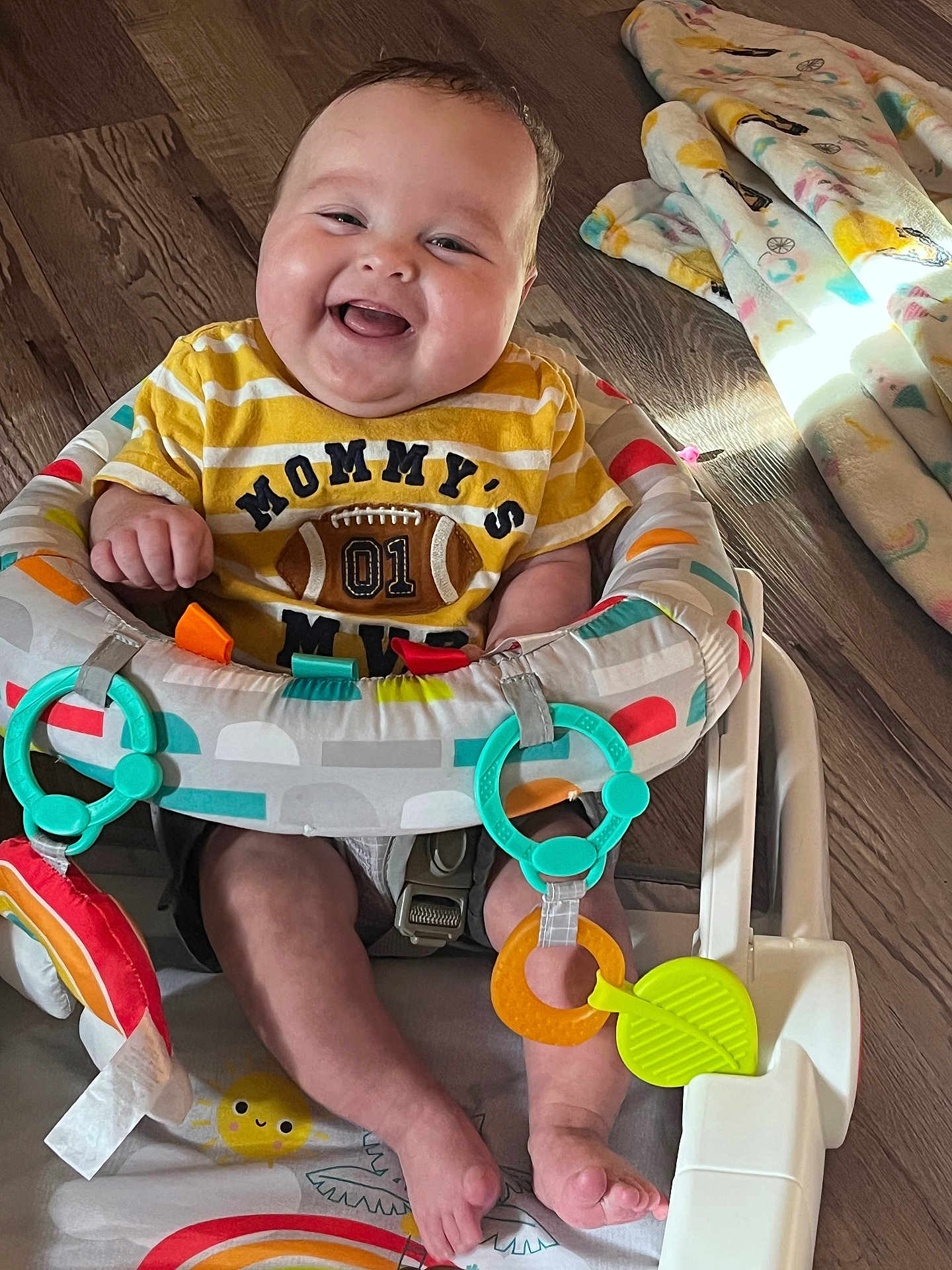 Kamden is registered to the contest to win money with this photo: baby, smiling, infant, child, toy, baby_seat, colorful, floor, blanket, happy, clothing, face, feet, indoors, play, cute, person, seat, wood_floor, teether