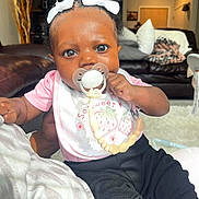 Audri joined the competition — help win amazing prizes! baby, infant, pacifier, hair_bows, pink_shirt, black_pants, living_room, couch, pillows, blanket, beads, child, cute, portrait, indoor, person, hand, skin, expression, comfort