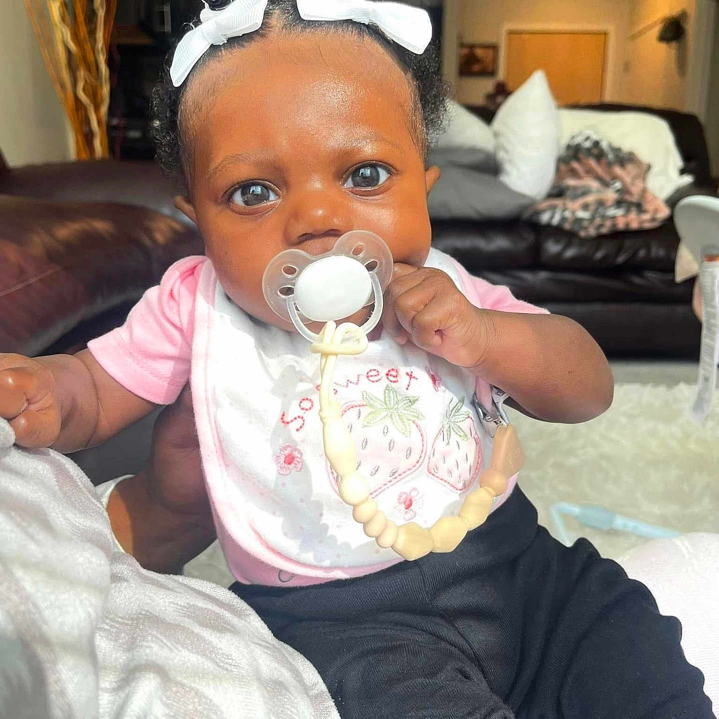 Audri joined the competition — help win amazing prizes! baby, beads, black_pants, blanket, child, comfort, couch, cute, expression, hair_bows, hand, indoor, infant, living_room, pacifier, person, pillows, pink_shirt, portrait, skin